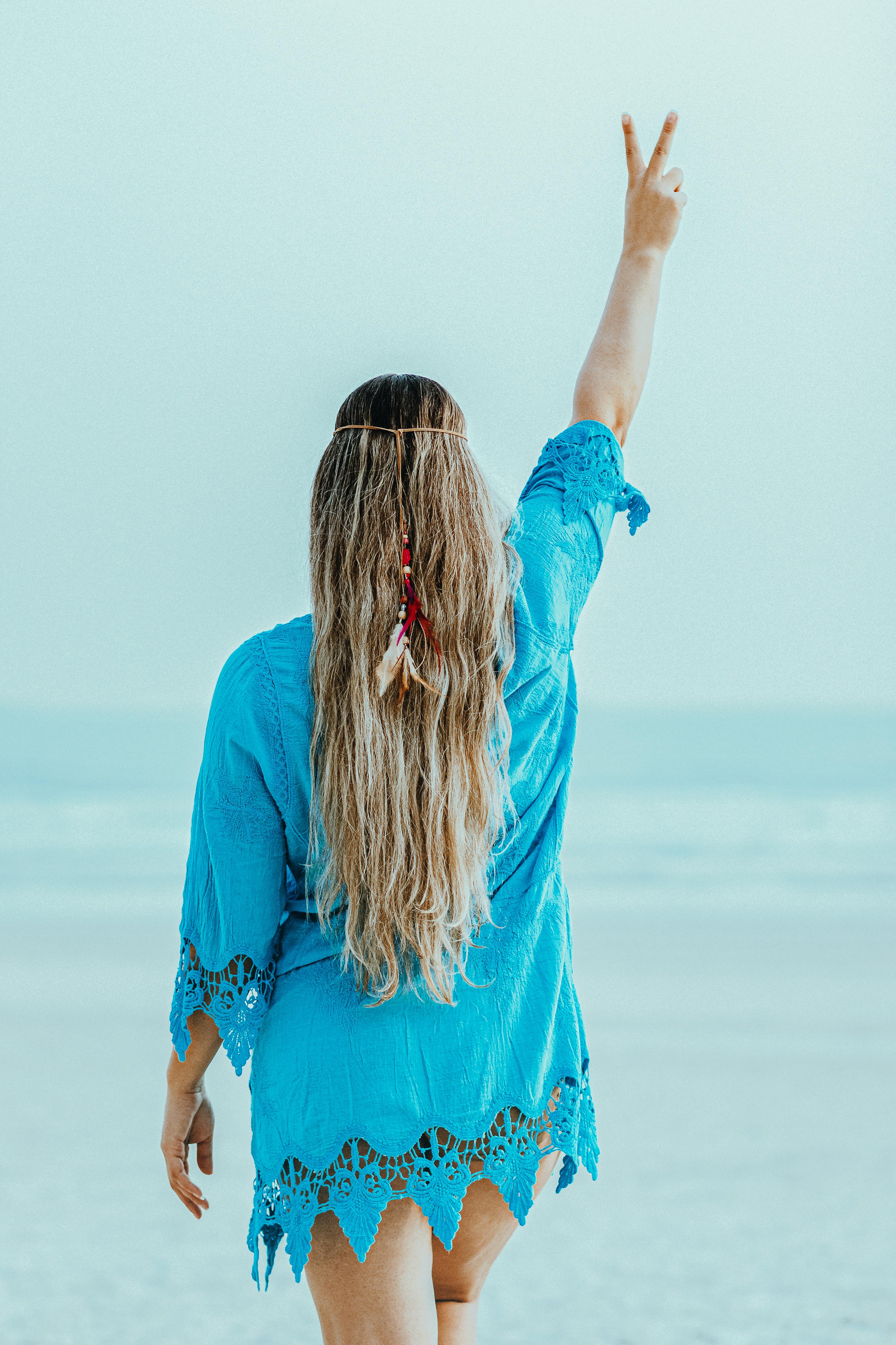 woman in blue dress wearing feather headwear doing peace sign