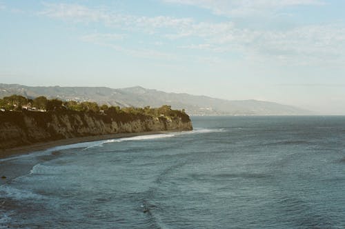 Body of Water Near Cliff under Blue Sky