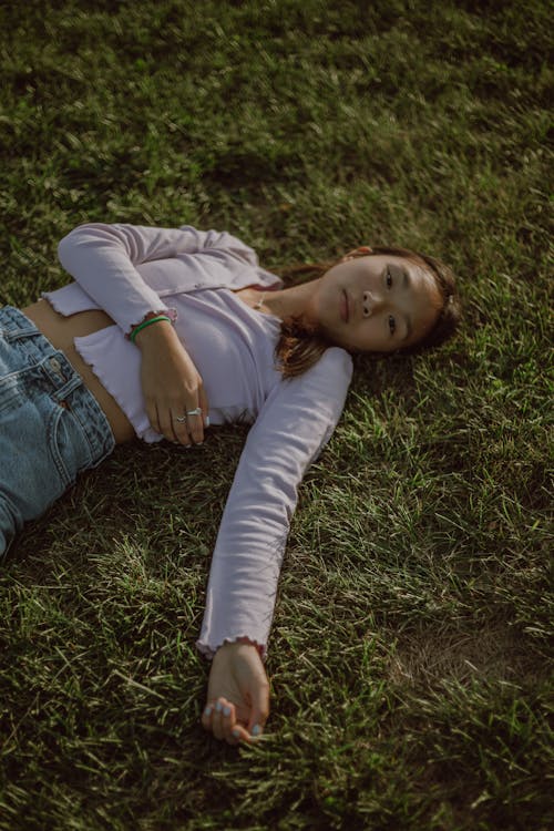 Free From above of Asian relaxed female lying on grassy ground while resting in solitude in nature Stock Photo