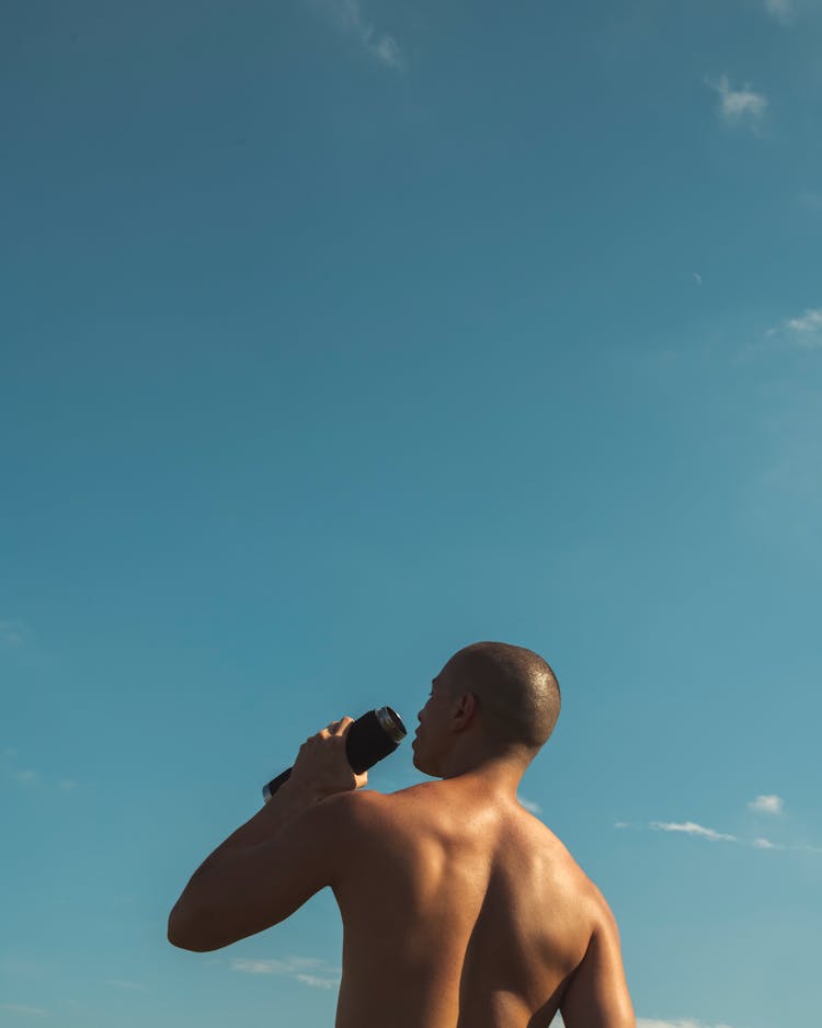 Shirtless Man Holding Black Water Tumbler Under Blue Sky