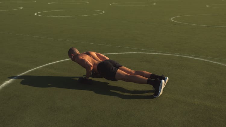 Man In Black Shorts Doing Push Ups On Green Field