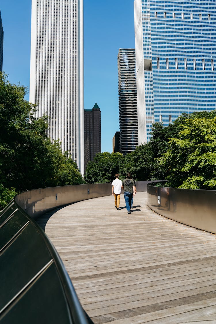 Unrecognizable People Walking On Boardwalk Towards City Skyscrapers