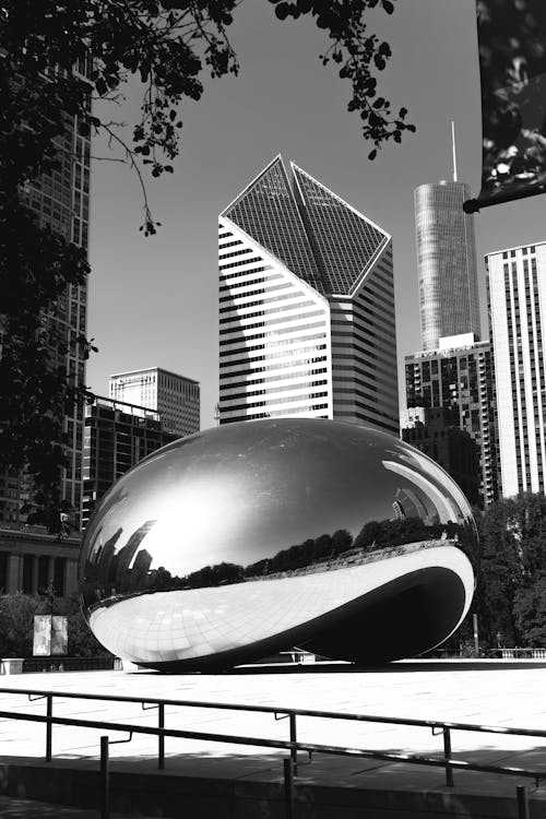 Black and white public sculpture of Cloud Gate representing big drop of mercury and located amidst contemporary futuristic Chicago city architecture