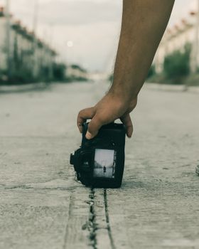A person holds a camera close to the ground on a city street, capturing the urban scene.