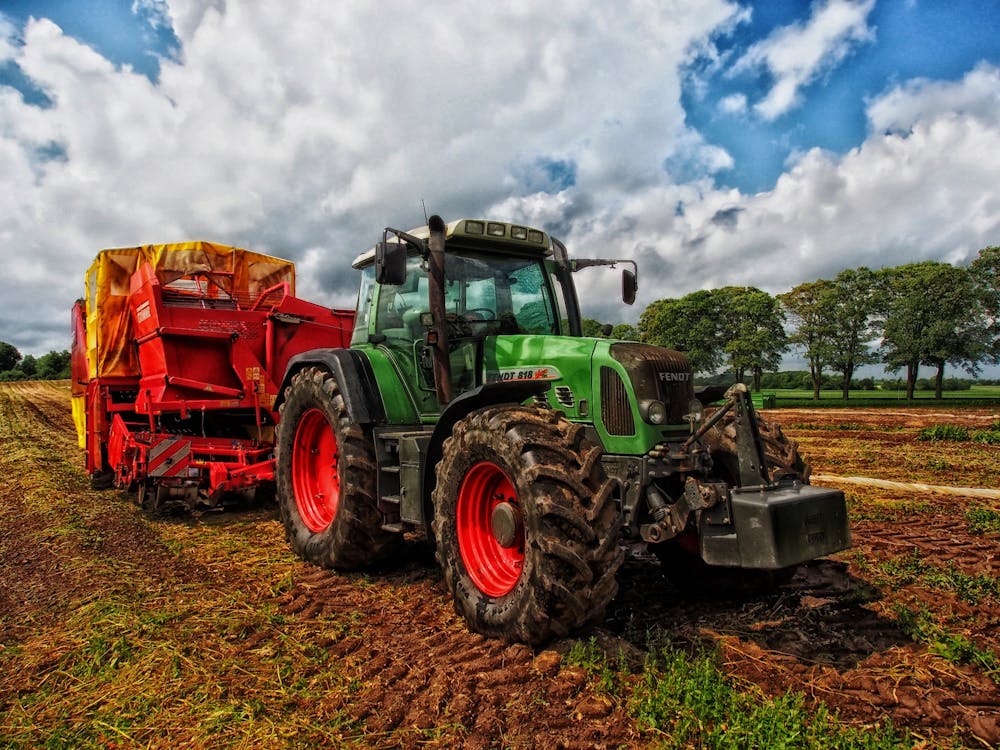 Green Tractor Pulling Red Bin on Field at Daytime