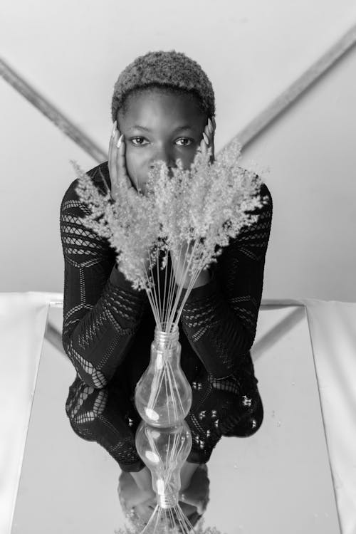 Free Calm young black woman sitting at table with mirror and flowers vase with hands on cheeks Stock Photo