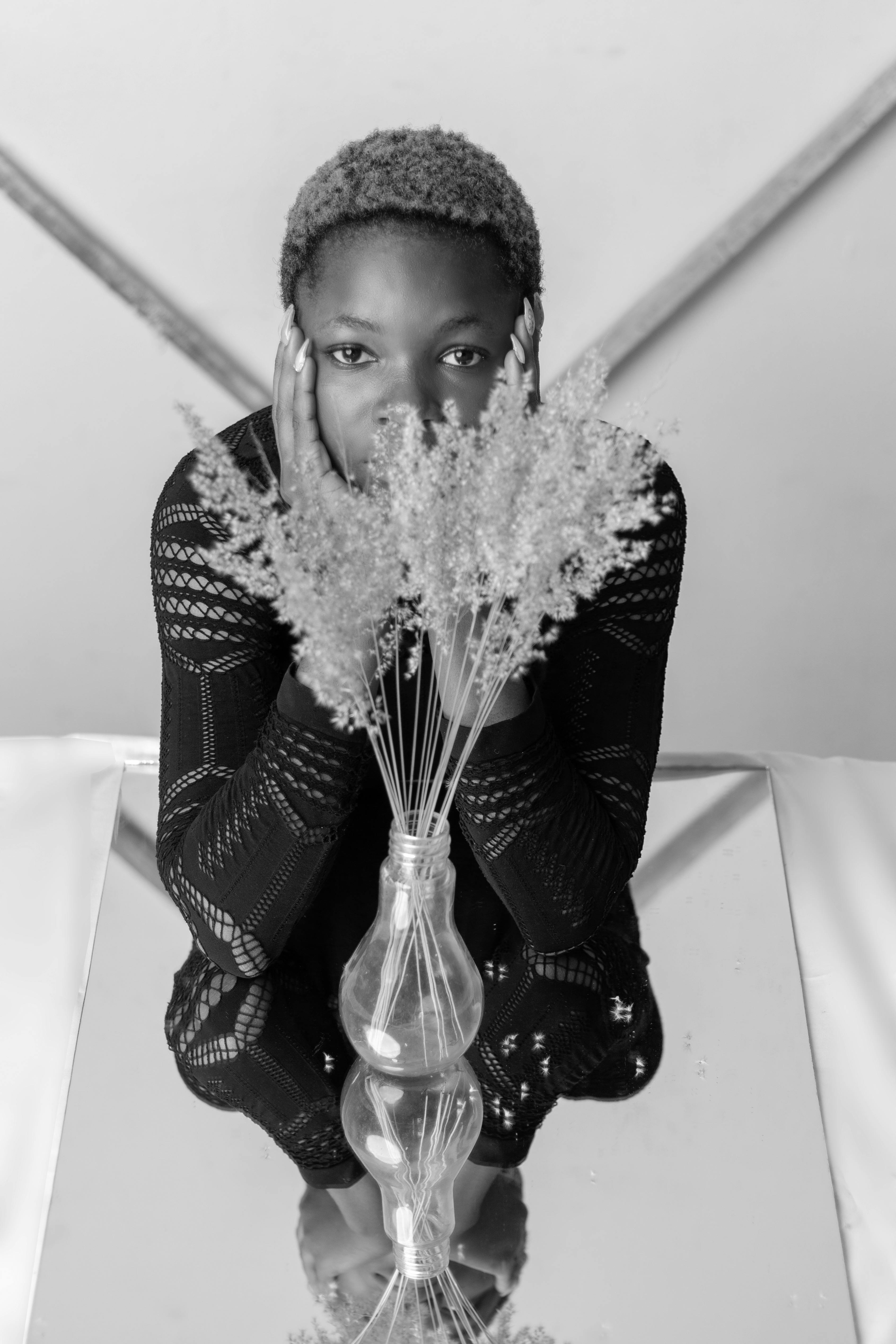Anonymous black woman sitting near flowers vase and window at home ...