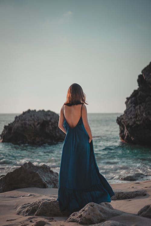 不可識別的女性女人穿著長裙站在岩石的海邊