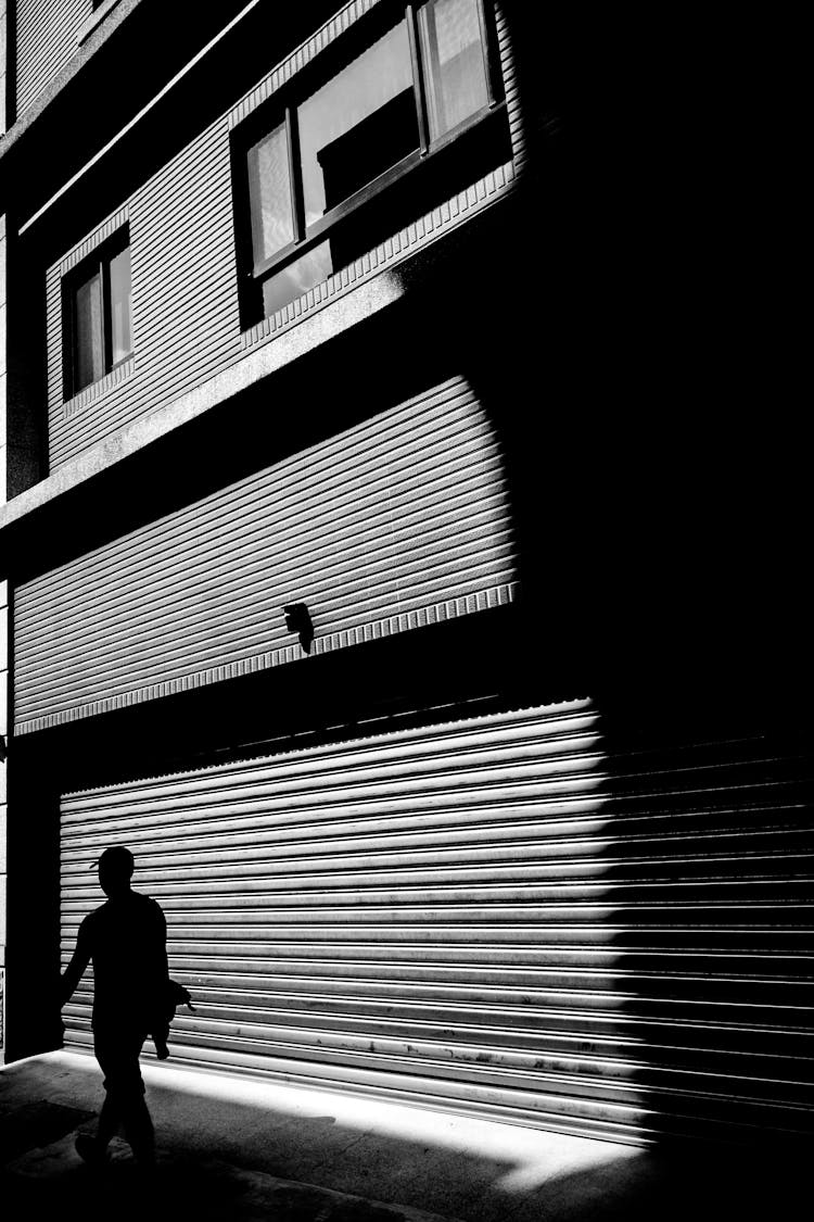 Silhouette Of A Person Walking Beside A Building