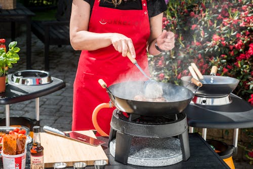 Photo of a Person in a Red Apron Cooking on a Black Pan