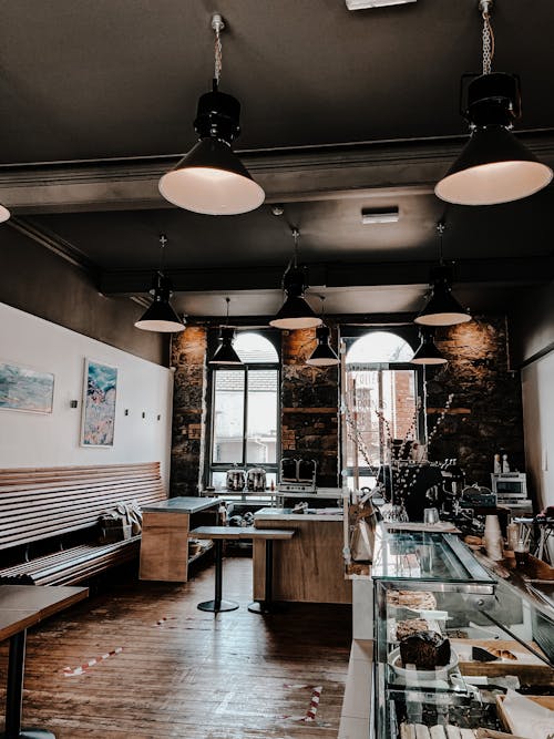 Interior of comfortable cafe with benches and tables near glass counter with different cakes