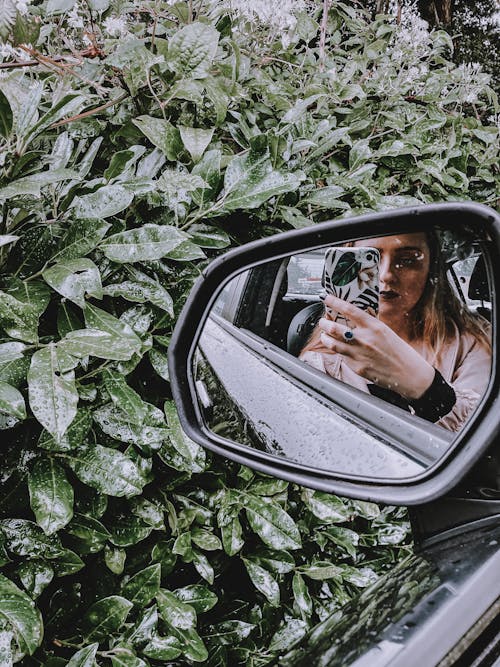 Young woman taking photo in mirror of car