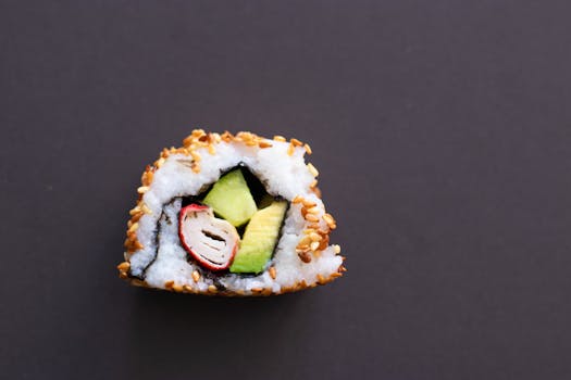 Close-up photo of a sushi roll featuring avocado and sesame seeds on a dark background.