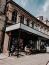 Exterior of old shabby aged cafe with group of people resting at tables under canopy