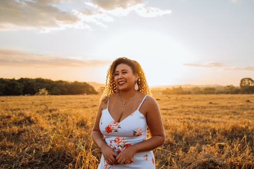 Happy ethnic woman smiling while standing in field at sunset