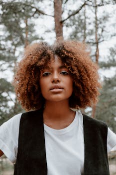 一位卷发的年轻女子自信地站在宁静的森林中