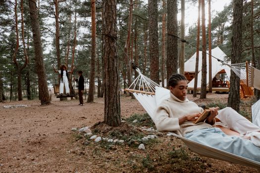 A man relaxes in a hammock reading a book in a tranquil forest setting.