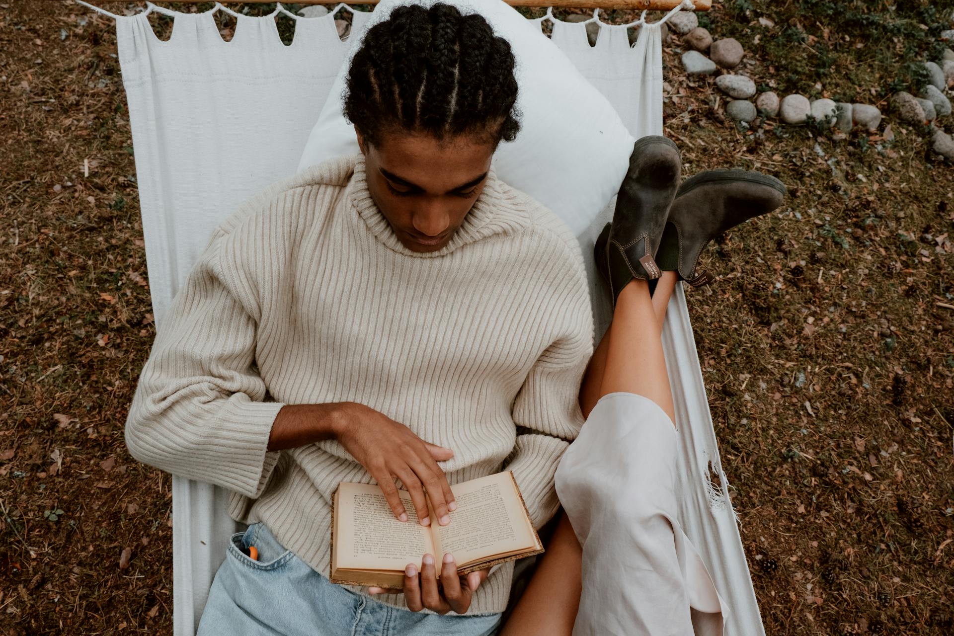 A man lounging in a hammock reading a book, enjoying leisure time outdoors.