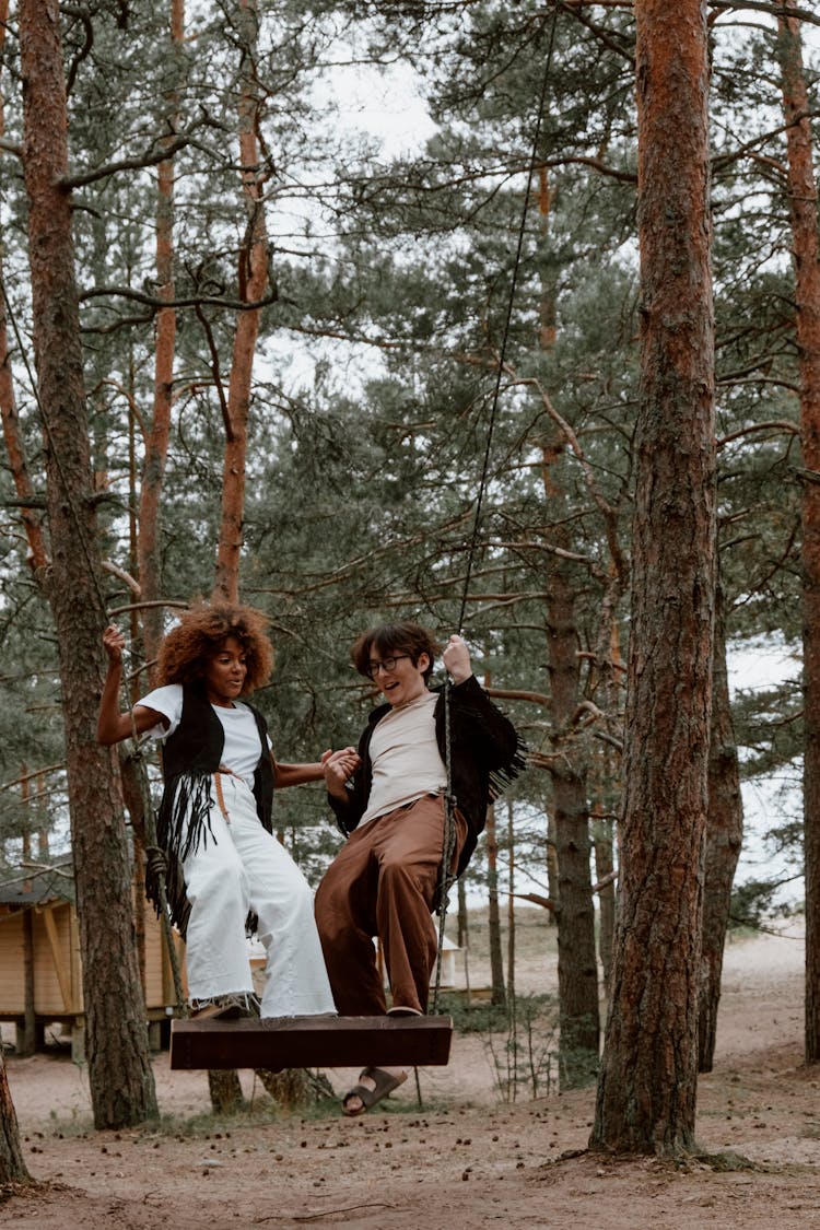 Young Man And Woman Standing On A Swing In The Forest