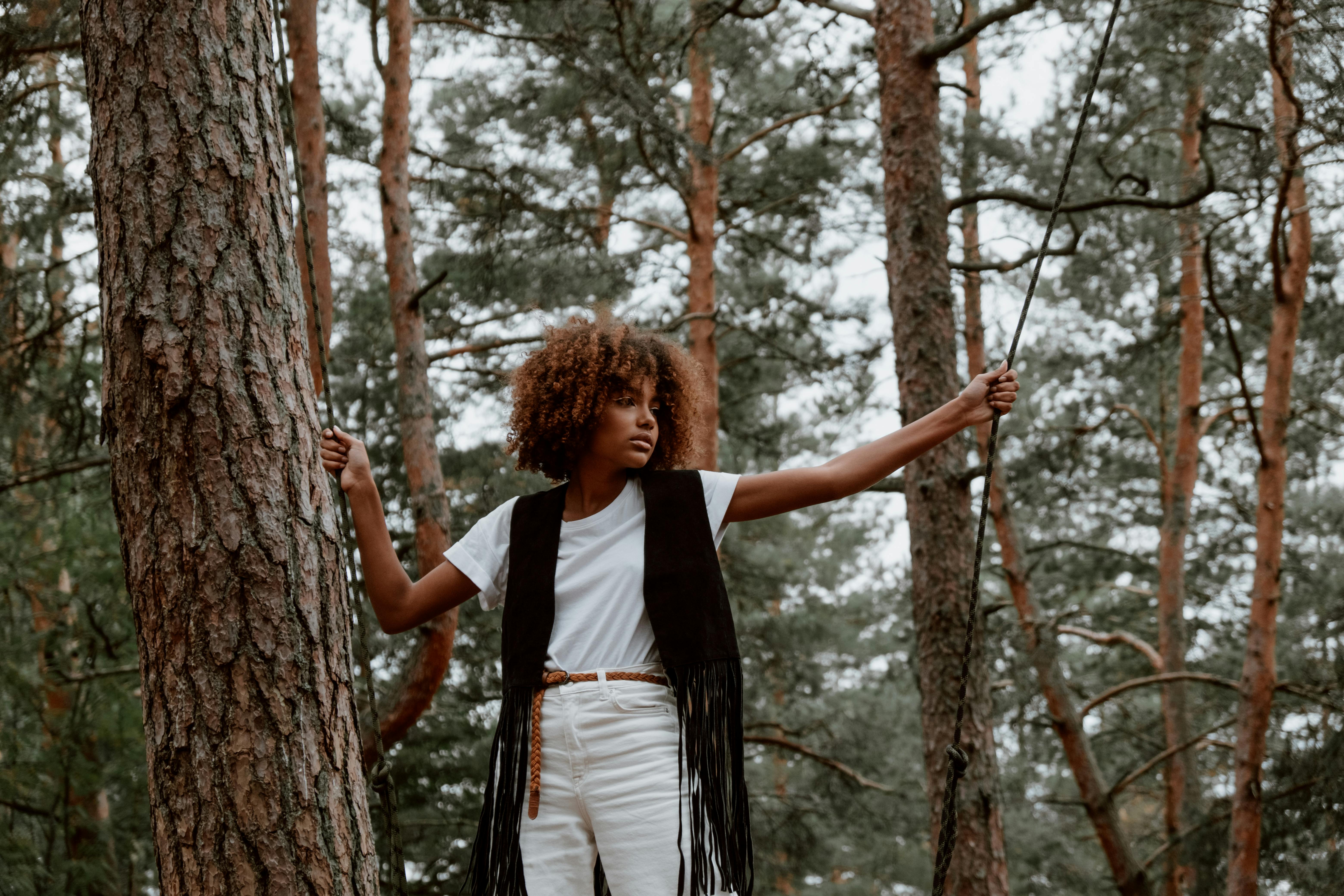 woman standing on a swing and holding onto the ropes in a forest