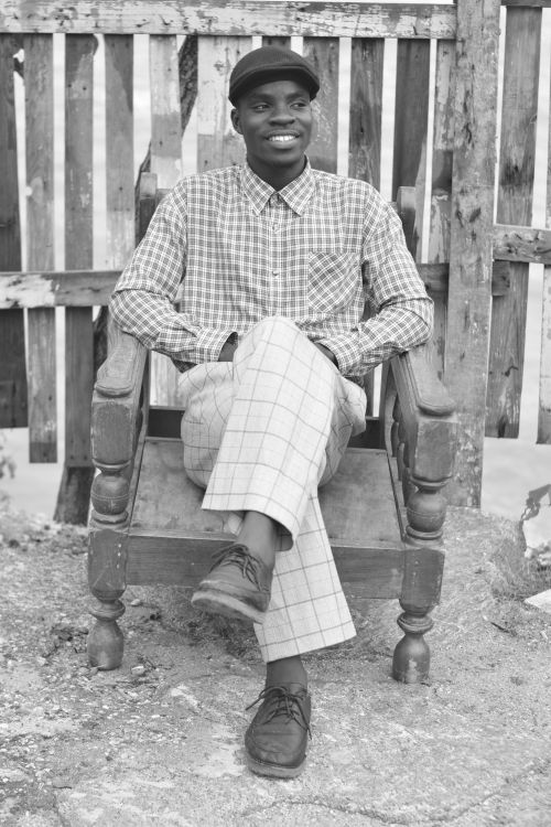 Free A man in casual attire sits in an old chair, smiling, with a fence background. Stock Photo