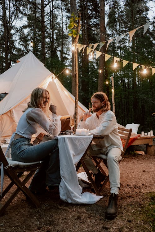 A Couple Sitting on Wooden Chairs Dining Near a Tent