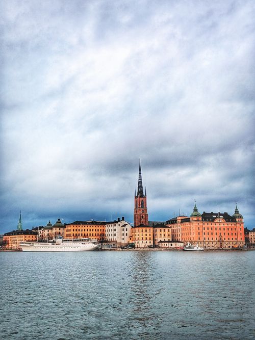 Free Beautiful view of Stockholm's old town waterfront and Riddarholmen Church under cloudy skies. Stock Photo