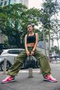Woman in Black Tank Top and Green Pants Sitting on Brown Wooden Seat