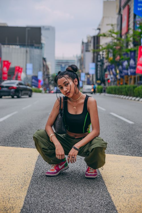 Free Trendy woman crouching on city street, showcasing urban fashion style. Stock Photo
