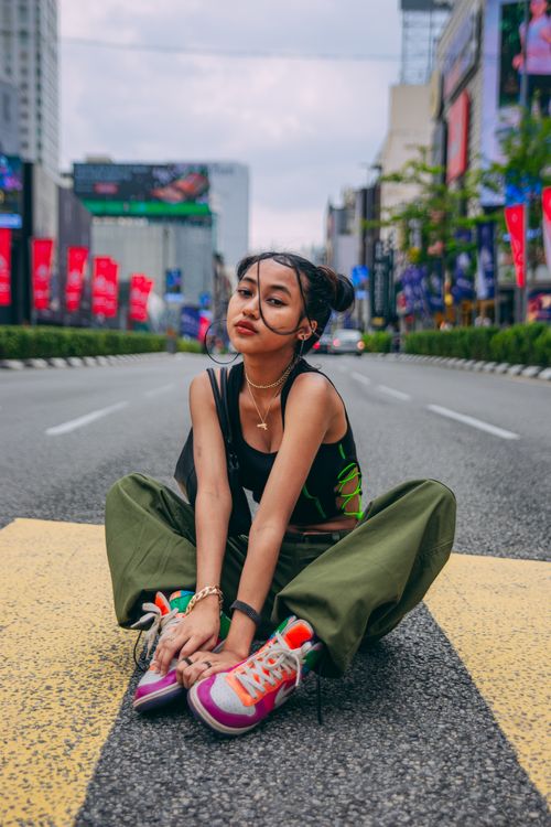 Free Stylish Asian woman posing seated on a city road, embracing modern street style. Stock Photo