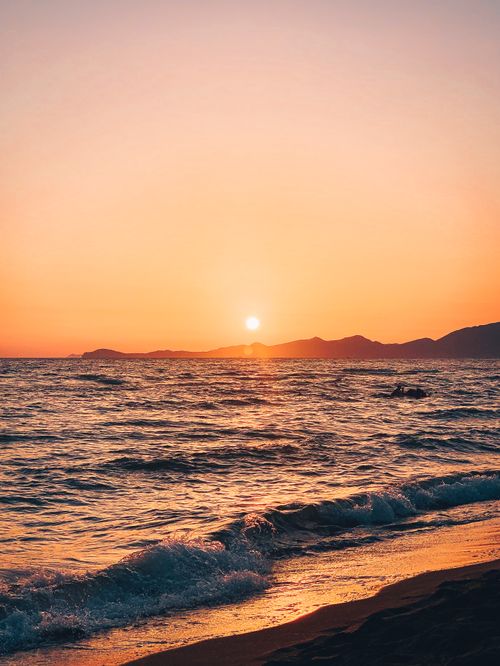 Free A picturesque sunset over calm waves and a serene shore, capturing the essence of nature's beauty. Stock Photo