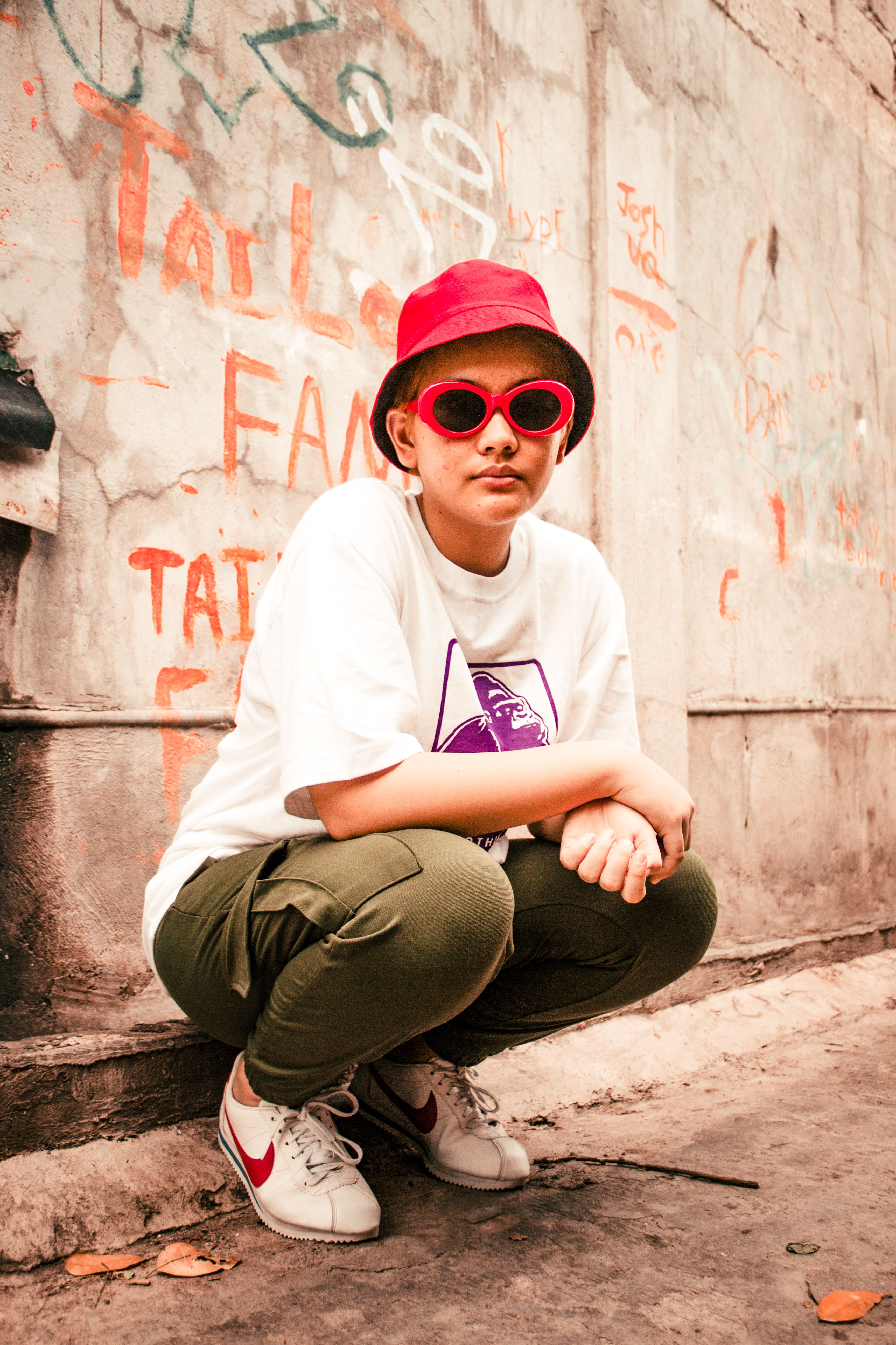 Young woman in urban setting wearing red hat and sunglasses, showcasing bold fashion style.