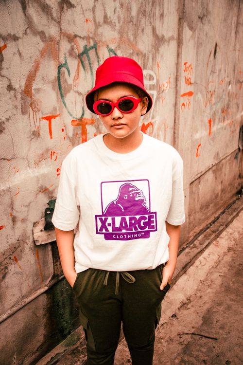 Free Stylish individual in streetwear, featuring a bold red hat and sunglasses against a graffiti backdrop. Stock Photo