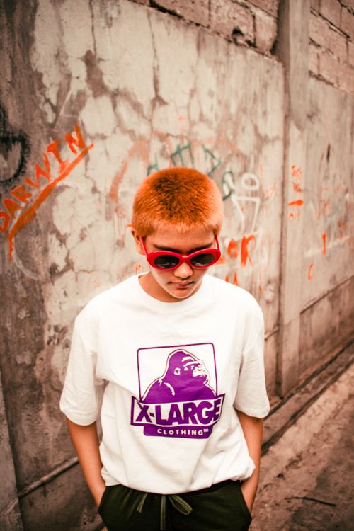 Free Young woman with red sunglasses and white t-shirt stands in urban setting. Trendy street fashion vibe. Stock Photo