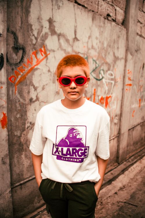 Free A stylish individual wearing red sunglasses and a graphic T-shirt poses against a graffiti wall. Stock Photo