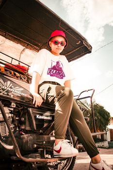 Stylish teenager in red hat and sunglasses sitting on a motorcycle outdoors.