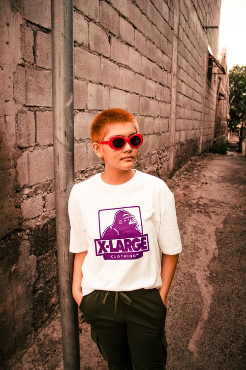 Free Fashionable young adult in white shirt with red sunglasses, poses in a rustic alleyway. Stock Photo