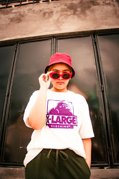 Free Fashionable young woman in urban streetwear posing with sunglasses and bucket hat for a modern portrait. Stock Photo