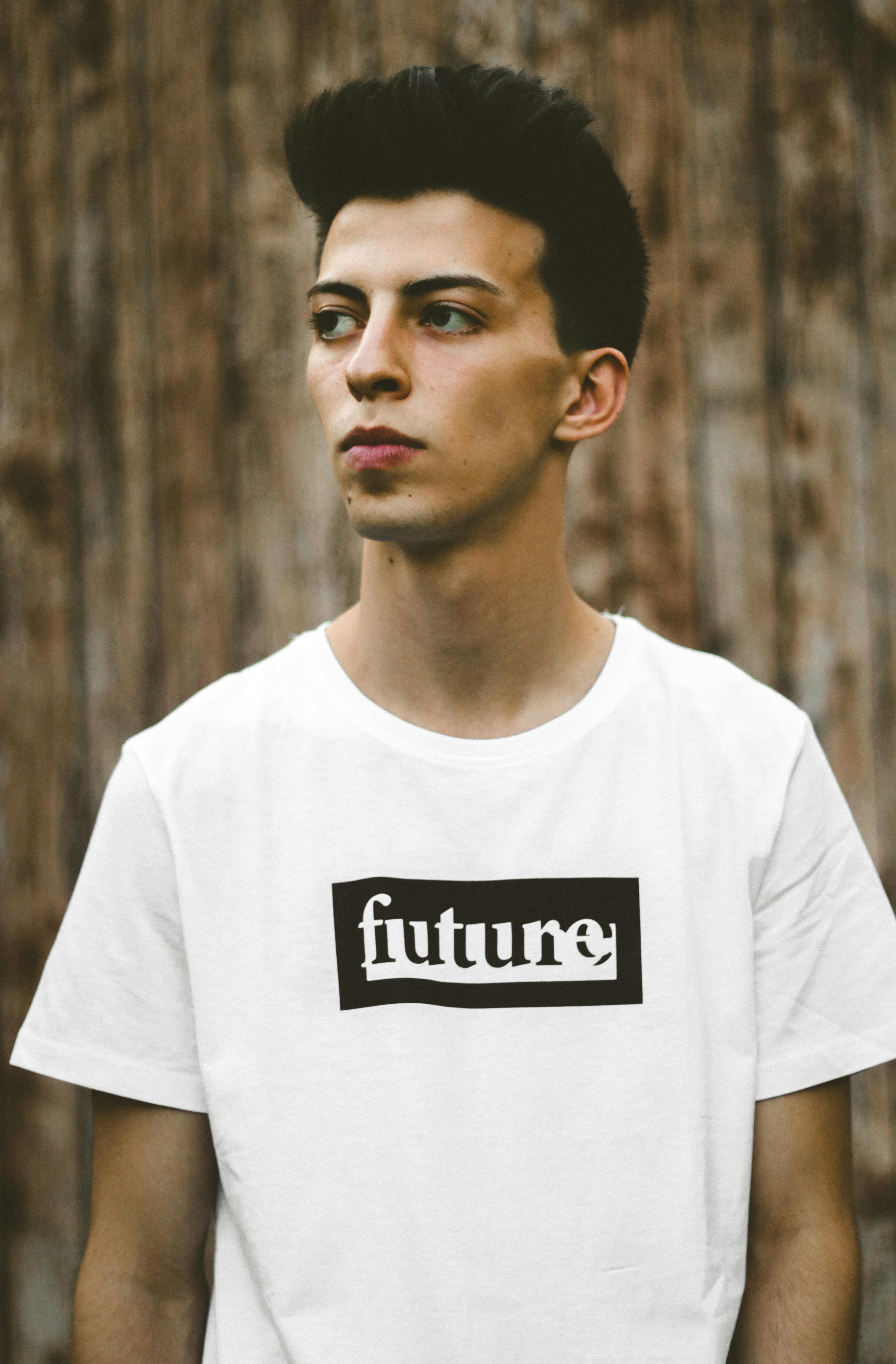 Casual portrait of a young man wearing a white t-shirt with future print, wooden background.