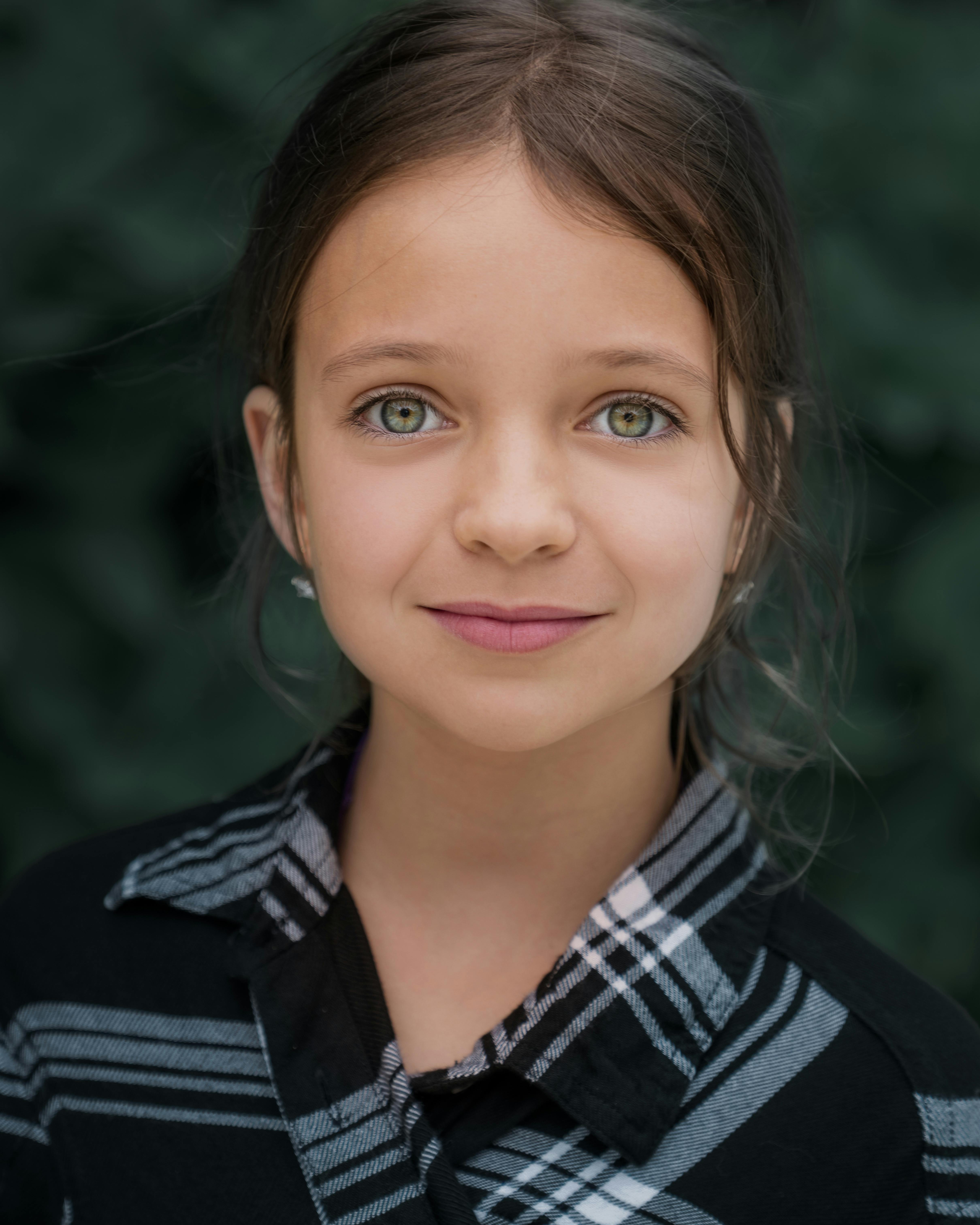 Friendly girl in casual outfit with brown hair looking at camera with sincere gaze on blurred background
