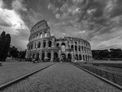 Black and white of historic Colosseum with tourists walking on paved square in Madrid