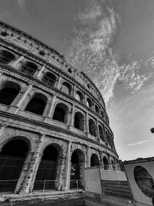 Black and white low angle of Colosseum with arched windows and fence for restoration in Rome