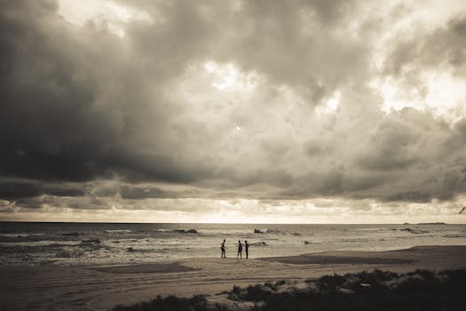 Silhouetted figures on a moody beach under dramatic clouds at sunset.