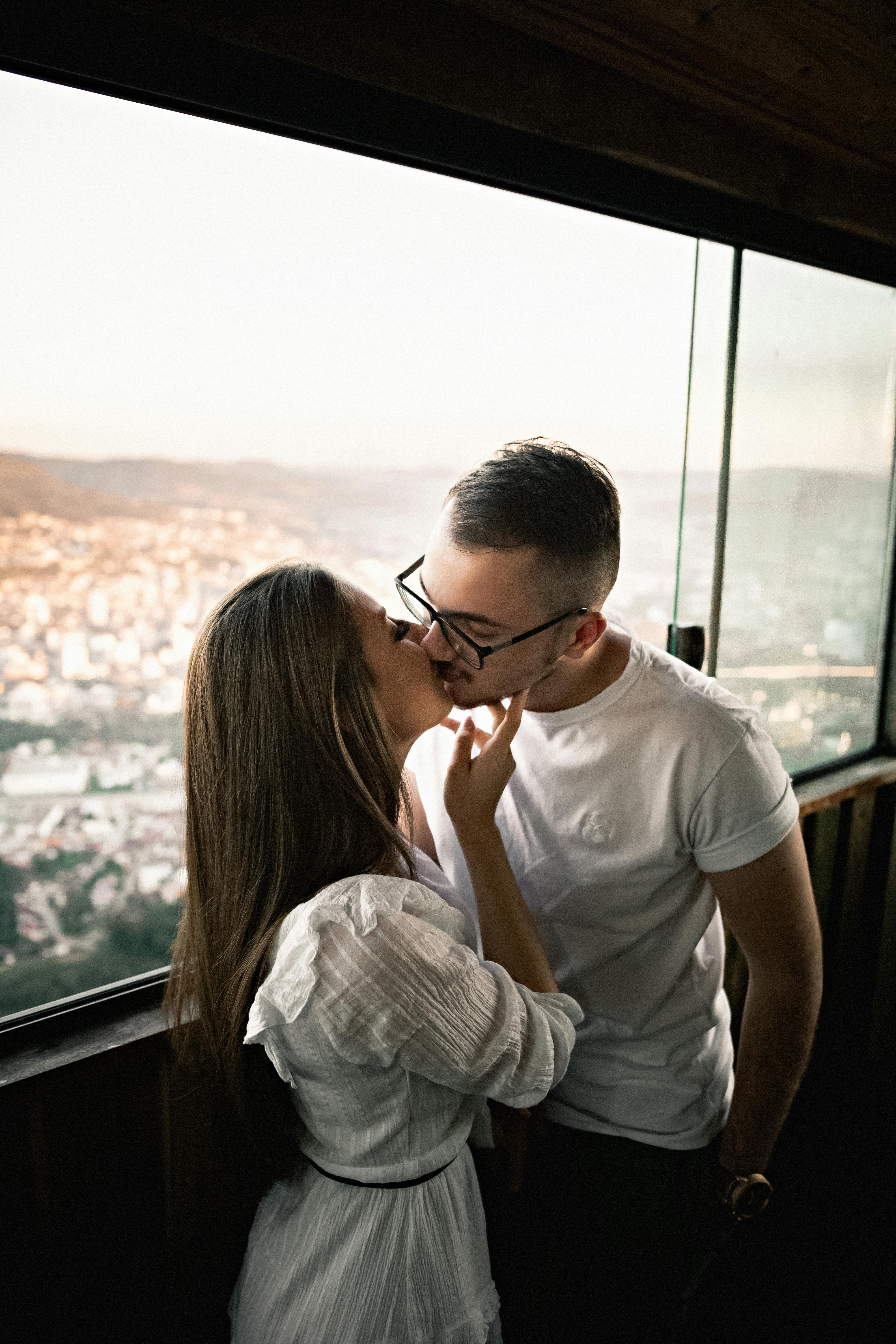 Young loving couple kissing gently standing near window · Free Stock Photo