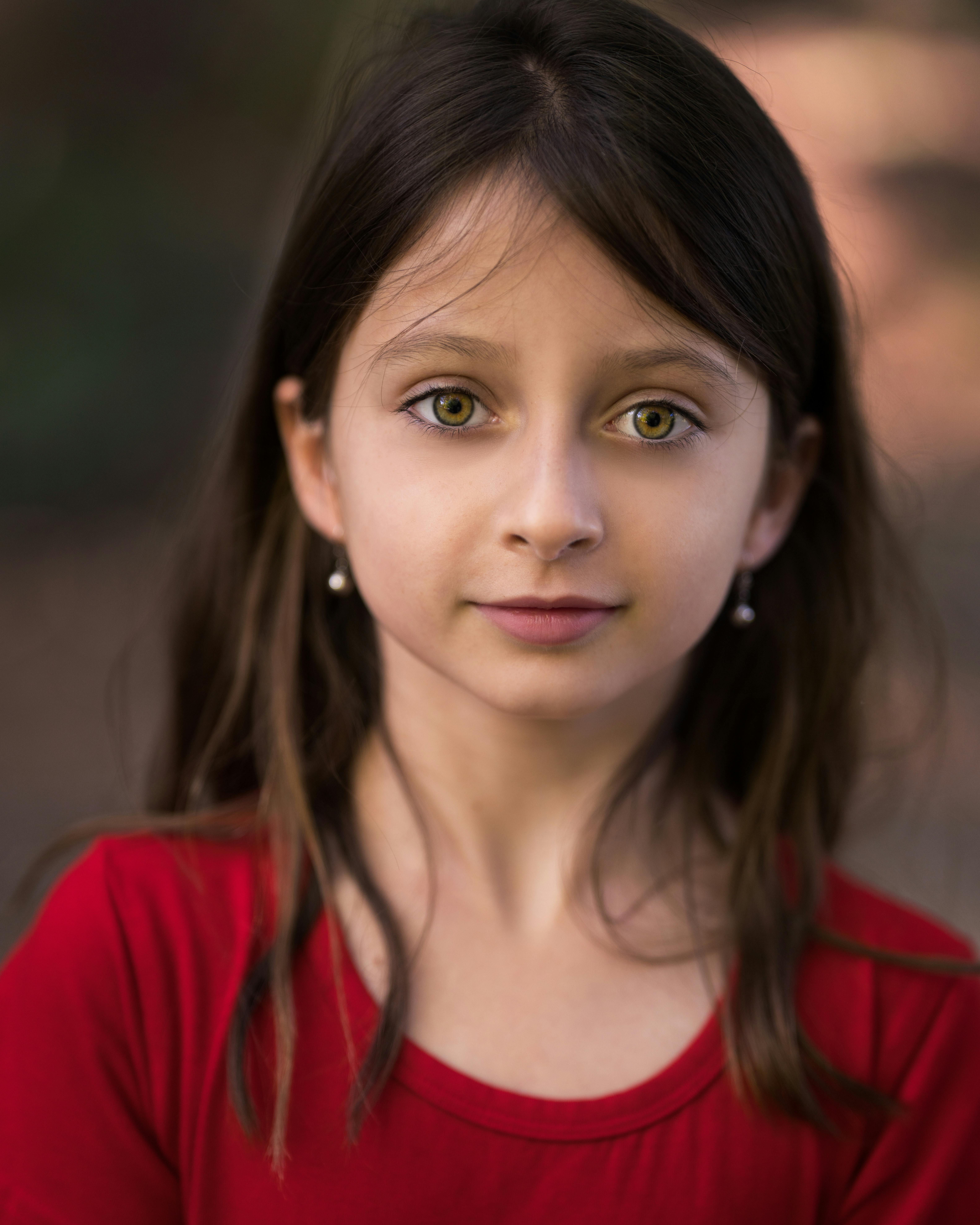Charming girl in red apparel with earrings and dark hair looking at camera in daytime