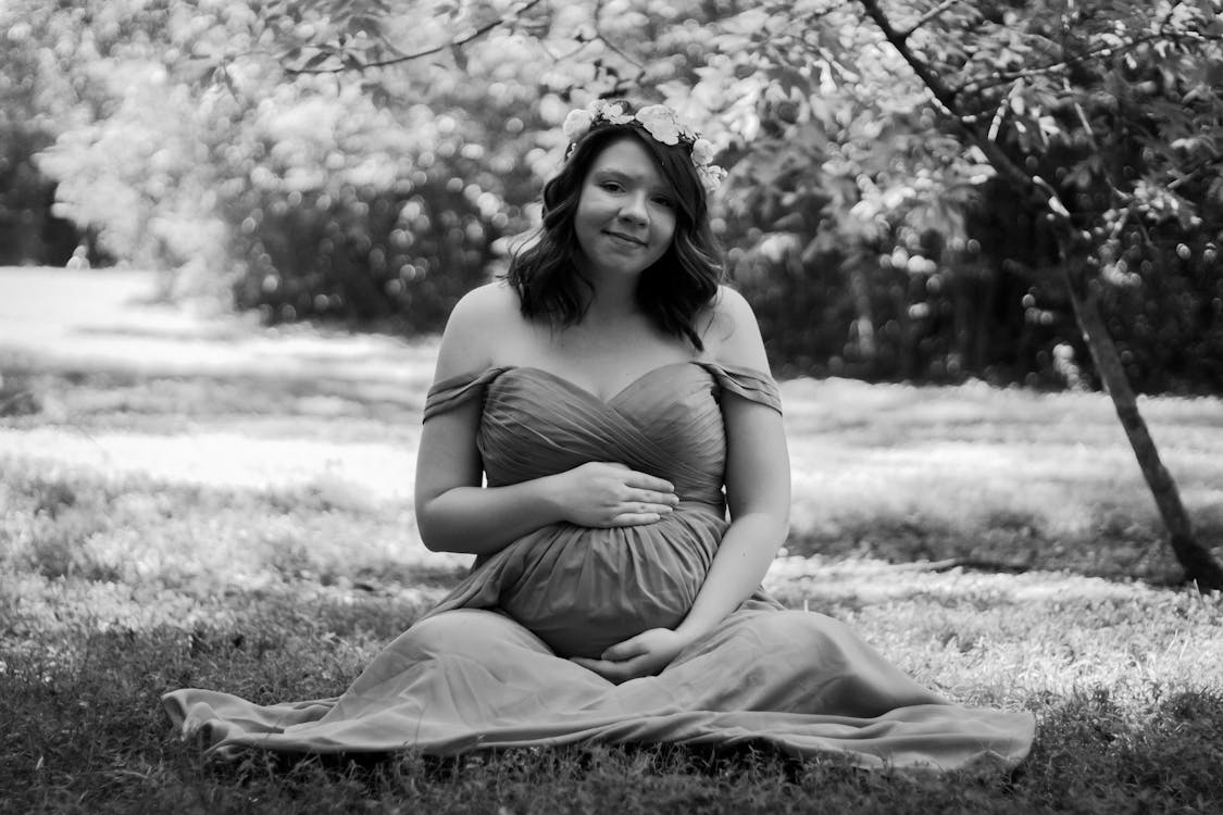 Grayscale Photo of a Pregnant Woman Sitting on Grass