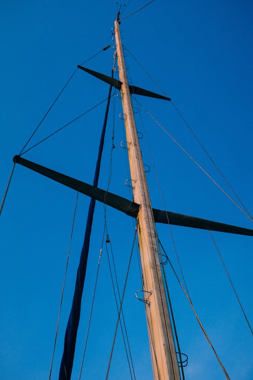 From below of wooden mast with ropes against blue sky in sunny weather in harbor in summer day in nature