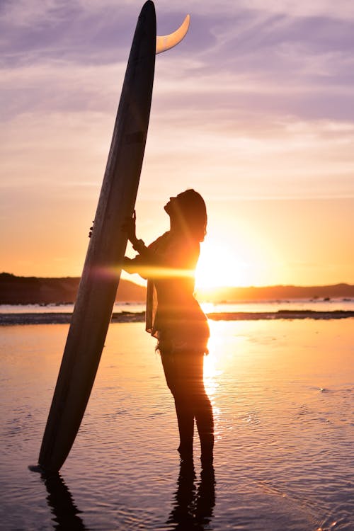 Silhouette of a Woman Holding a Surfboard on the Beach during Sunset