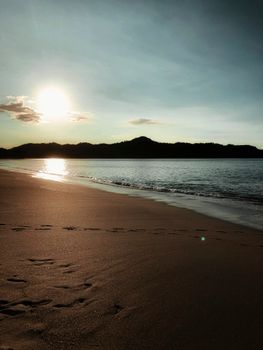 Peaceful sunrise on a Costa Rican beach with gentle waves and footprints in the sand.