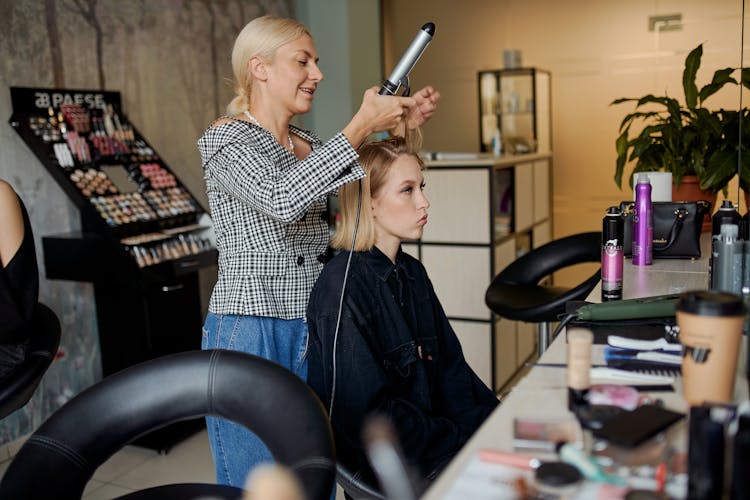 Smiling Hairdresser Straightening Hair Of Female Client